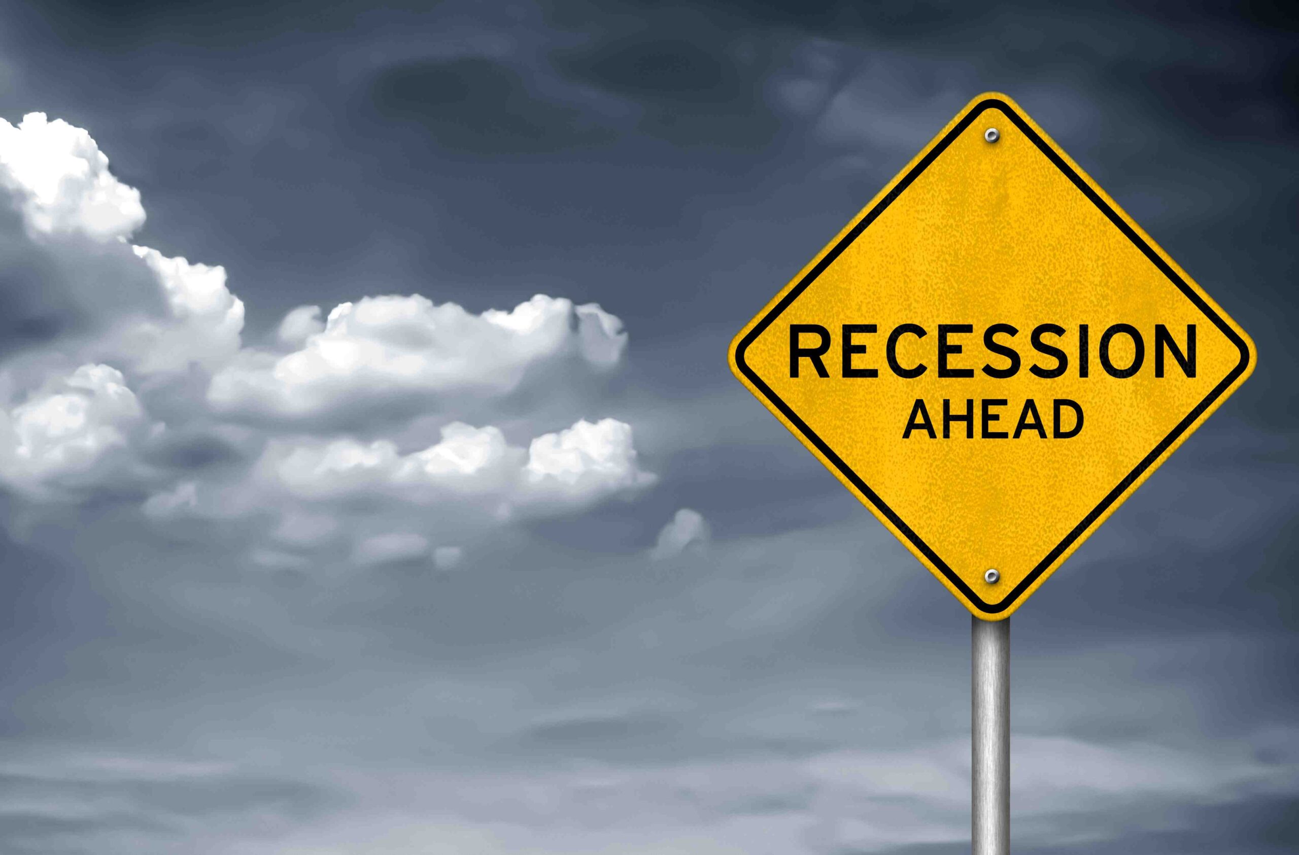 A yellow road sign that says "recession ahead" pictured with a stormy background.